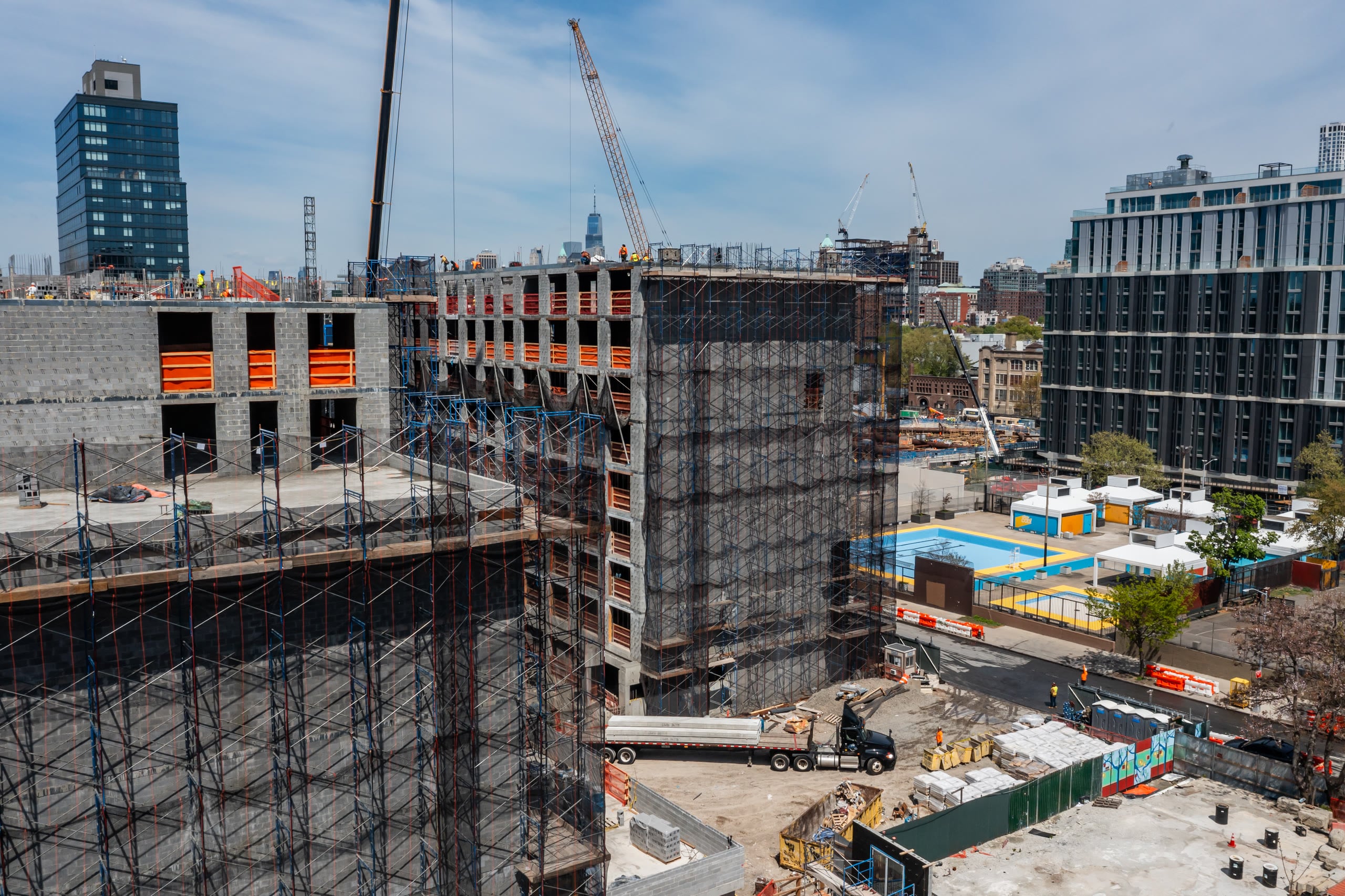 Aerial view of two precast buildings under construction with cranes and the Manhattan skyline behind