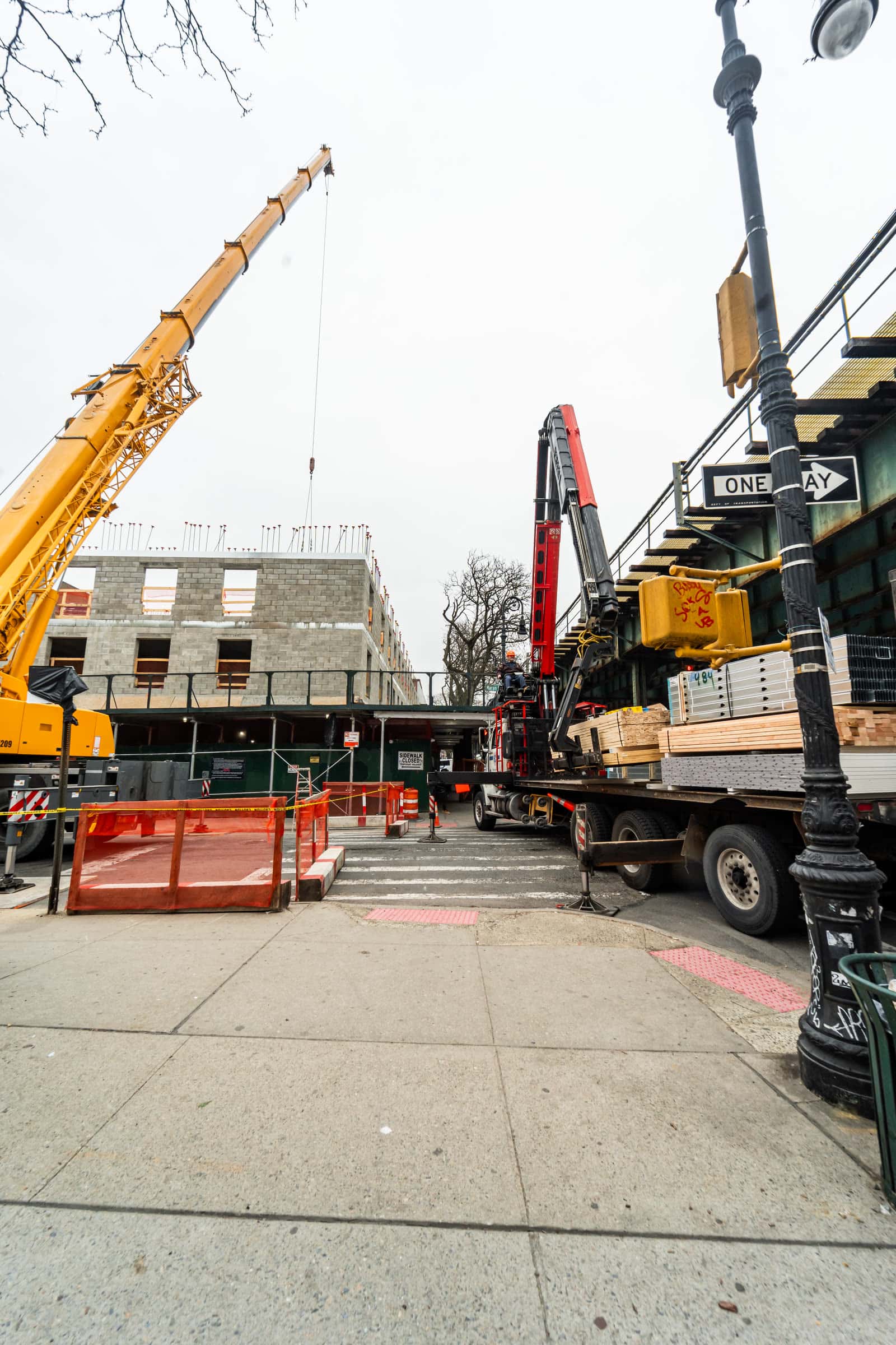 Crane and boom truck delivering material under an elevated subway line