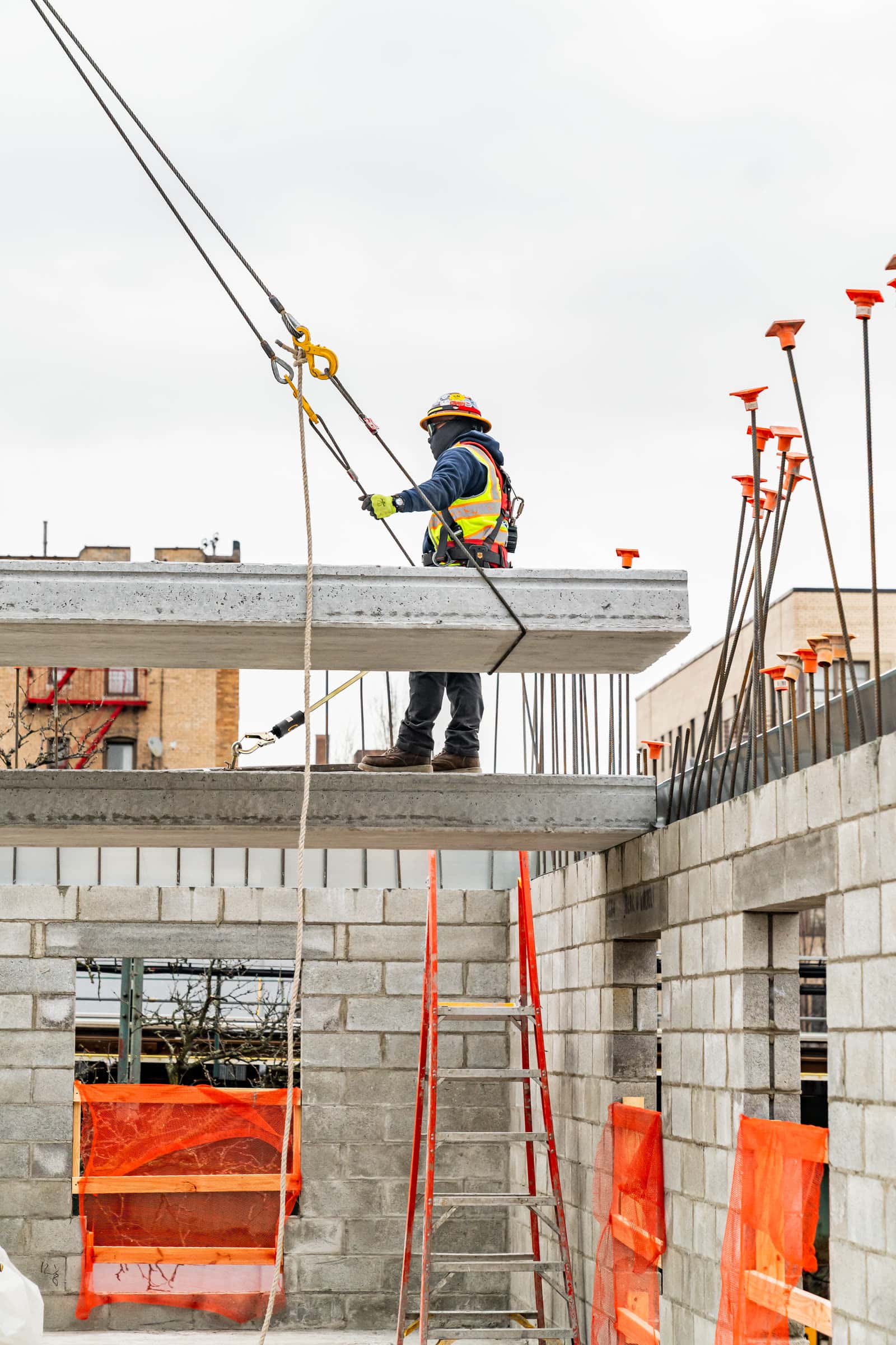 Harnessed worker guiding crane rigging at a plank edge